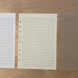 May include: Three sheets of lined paper with punched holes on the left side. The paper is white, cream, and brown. The text on the paper reads "Happy Planning Days".