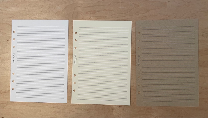 May include: Three sheets of lined paper with punched holes on the left side. The paper is white, cream, and brown. The text on the paper reads "Happy Planning Days".