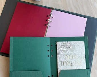 May include: A green binder with a red and pink insert and a pocket on the front. The pocket contains a small notebook with the words "Gone Traveling" on the cover.