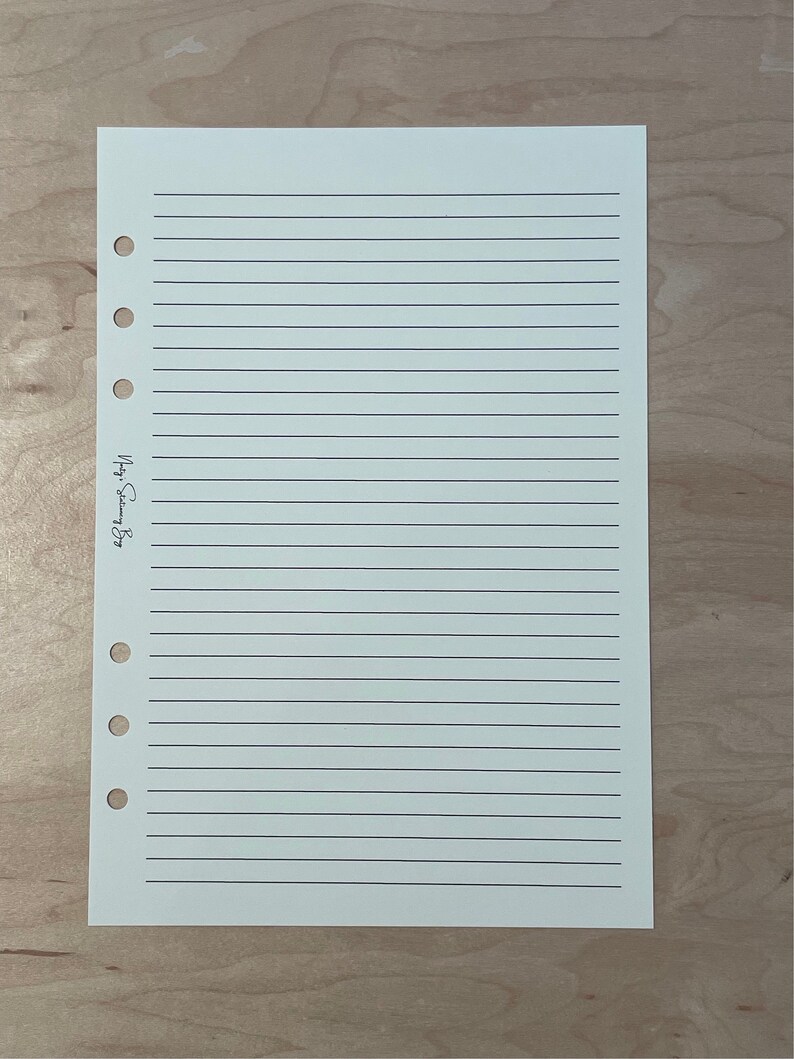 May include: A blank, lined, white paper sheet with a hole punch on the left side. The paper is for a planner or journal.
