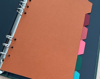 May include: A green binder with a brown paper insert and colorful tab dividers. The binder has a silver ring mechanism and is closed.