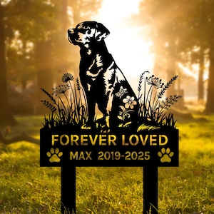 Può includere: Paletto da giardino in metallo nero con silhouette di cane, dettagli floreali e la scritta "FOREVER LOVED MAX 2019-2025" con impronte di zampe. Il cane è seduto nell'erba. Lo sfondo mostra alberi e luce solare sfocata.
