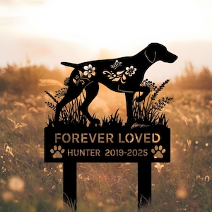 Può includere: Paletto commemorativo per cani in metallo nero con le parole "FOREVER LOVED" e "HUNTER 2019-2025". La silhouette del cane è decorata con motivi floreali. Il paletto è in un campo di erba alta con un tramonto sullo sfondo.