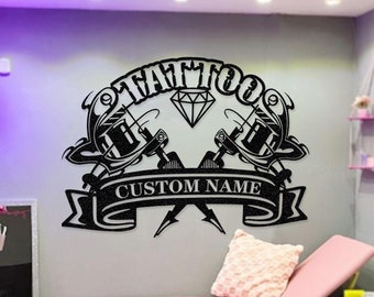 May include: Black and white tattoo parlour sign with two crossed tattoo guns and a diamond. The sign says "Tattoo" and "Custom Name".