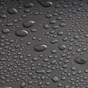 May include: Close-up of a dark gray surface covered in water droplets of varying sizes. The droplets reflect light, creating highlights and shadows. The surface appears smooth, with a subtle texture visible.