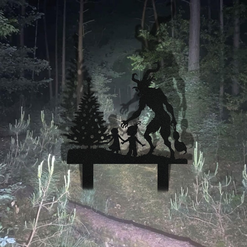 May include: Black metal yard art depicting a Krampus figure with children and a Christmas tree in a forest setting. The silhouette shows the horned Krampus reaching towards the children, with a dark forest background.