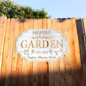 May include: White metal garden sign with the text "Melissa's Garden Est. 2024  Veggies, Flowers, Herbs" and decorative cutouts of butterflies, a watering can, and a wheelbarrow.