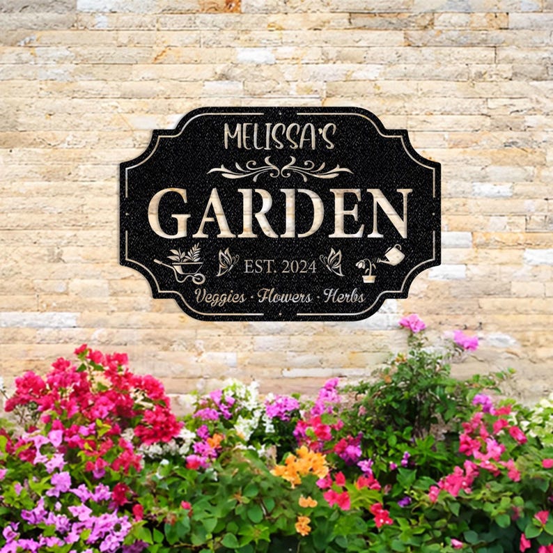May include: Black garden sign with white text that reads "Melissa's Garden Est. 2024 Veggies - Flowers - Herbs".