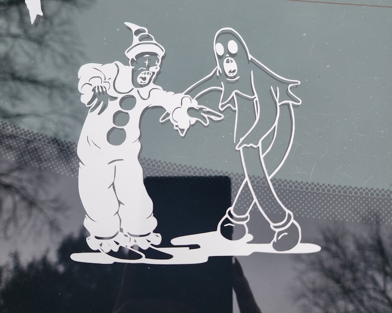 May include: A white vinyl sticker featuring a cartoon clown and ghost. The clown is wearing a hat and has a wide smile. The ghost has a large mouth and two eyes. The sticker is on a gray background.