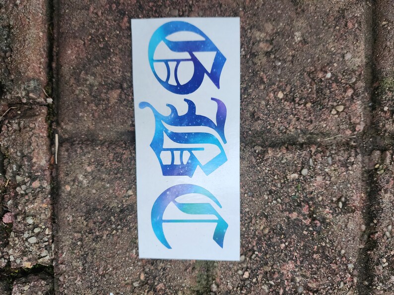May include: A white sticker featuring three stylized letters in a gradient of blue and purple, resembling a celestial design. The letters are in a unique, ornate font, with a space-themed aesthetic.