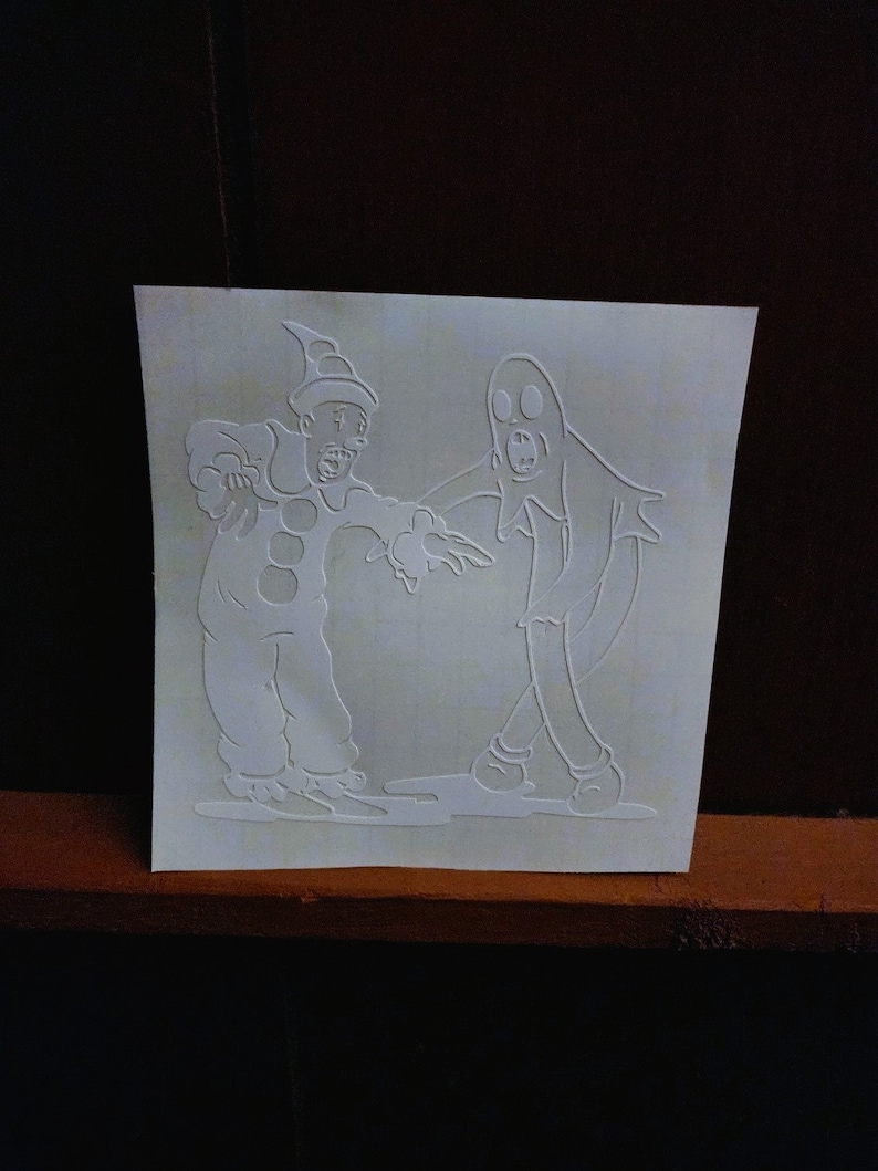 May include: A white vinyl sticker featuring a cartoon ghost and a clown. The ghost is wearing a sheet and has a surprised expression. The clown is wearing a hat and a costume with a large red circle on the front. The sticker is perfect for adding a spooky touch to any Halloween decor.