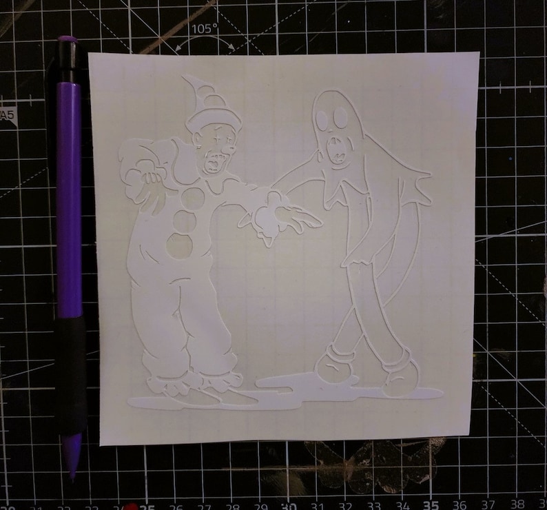 May include: A white vinyl stencil of a ghost and a clown. The ghost is wearing a sheet and has a surprised expression. The clown is wearing a traditional costume with a hat and a big smile.