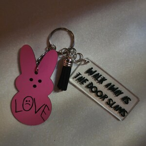Op de afbeelding: Roze konijnvormige sleutelhanger met een zwarte kwast en een transparante acrylbedel met de tekst "Walk Away Is The Door Slams".