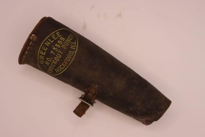May include: A vintage leather tool pouch, dark brown in color, with a riveted construction. The pouch features a metal clasp and a label that reads "GREENLEE NO. 73588 KNOCKOUT PUNCH ROCKFORD, ILL."