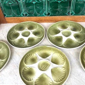 Könnte beinhalten: Ein Set aus sechs olivgrünen Keramik-Austernplatten. Jede Platte hat sechs muschelförmige Fächer und einen zentralen Brunnen. Die Platten haben eine glänzende Oberfläche und sind auf einer hellen Oberfläche angeordnet.