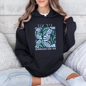 May include: Black hooded sweatshirt with a floral design and the text "nir oz" and "kibbutz nir oz" in white.