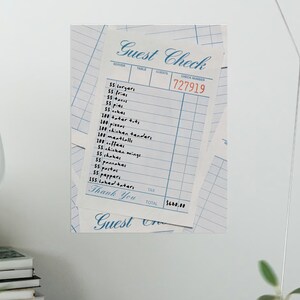 Könnte beinhalten: Nahaufnahme eines Restaurantbelegs mit blauem Rastermuster und dem Schriftzug "Guest Check" in eleganter Schrift. Der Beleg listet verschiedene Speisen und eine rote Rechnungsnummer auf. Die Worte "Thank You" sind ebenfalls sichtbar.