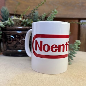 May include: White ceramic coffee mug with a red Nintendo-style logo that says "Noenti".