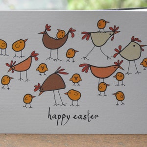 May include: A greeting card with a hand-drawn illustration of chickens and chicks. The card is white with a grey background and features the text "happy easter" in orange.