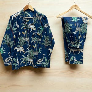Può includere: Completo pigiama blu navy con stampa a tema giungla. Il set comprende una camicia con bottoni e pantaloni abbinati, entrambi decorati con un motivo di leopardi, zebre, uccelli e fogliame tropicale. Bordatura bianca sui bordi.