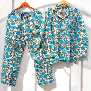 May include: A floral patterned pajama set. The set comprises a long-sleeved shirt and drawstring trousers. The design features blue flowers and brown vines on a white backdrop.