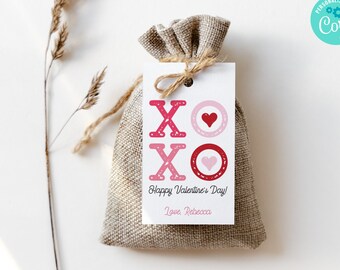 May include: A white gift tag with pink and red XOXO letters and hearts. The tag is tied with twine to a small burlap bag. The tag reads "Happy Valentine's Day! Love, Rebecca."