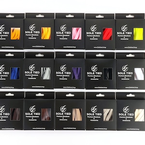 Pode incluir: Uma exibição de 15 caixas contendo cadarços em várias cores, incluindo amarelo, vermelho, rosa, azul, cinza, preto, marrom e bege. Cada caixa apresenta o logotipo "SOLE TIED" e o texto "Premium Shoelaces & Accessories".