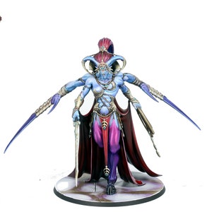 May include: A blue and purple painted miniature figurine of a female demon with four arms, wearing a red and gold robe and holding a sword. The figurine is standing on a circular base.