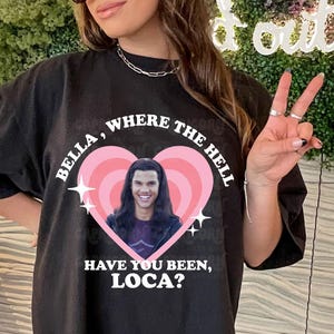 May include: Black t-shirt featuring a graphic of a person within a pink heart, with the text "BELLA, WHERE THE HELL HAVE YOU BEEN, LOCA?". The shirt also has the text "digital download", "png file", and "commercial use". The shirt is worn by a person wearing sunglasses and a black cap.