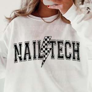 May include: White sweatshirt with black text that reads "Nail Tech" with a black and white checkered lightning bolt graphic.
