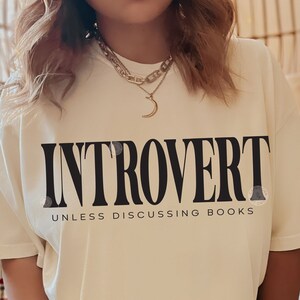 Pode incluir: Uma camiseta branca com o texto "Introvertido a menos que se discuta livros" impresso em preto.