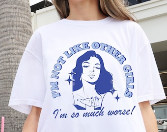 May include: White t-shirt with a blue graphic that reads "I'M NOT LIKE OTHER GIRLS, I'm so much worse!" The graphic features a woman blowing a kiss. The shirt is a casual, oversized fit.