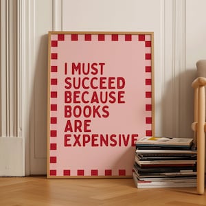 May include: A pink framed poster with a red checkered border. The poster has the text "I MUST SUCCEED BECAUSE BOOKS ARE EXPENSIVE" in red letters.