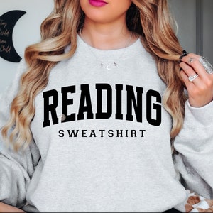 Könnte beinhalten: Ein grauer Pullover mit dem Text "READING SWEATSHIRT" in Schwarz.