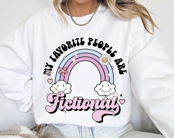 Op de afbeelding: Witte sweatshirt met een kleurrijke afbeelding. Het ontwerp toont een regenboog met de woorden "My Favorite People Are Fictional" in een retro lettertype. Inclusief lachende wolken, bloemen en harten.