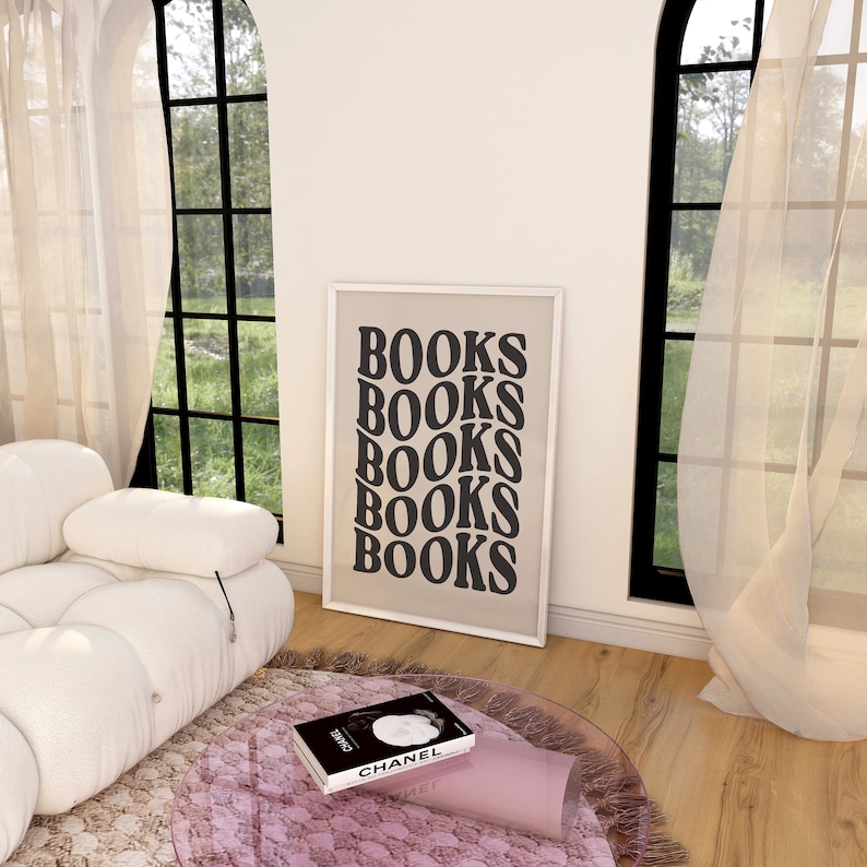 May include: A white couch with a black framed poster that says "BOOKS" five times. A pink and white rug is on the floor in front of the couch. A book with a black and white photo of a woman on the cover is on a pink glass table.