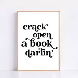 May include: A black and white printable wall art print with the text "crack open a book darlin'" in a retro font style.