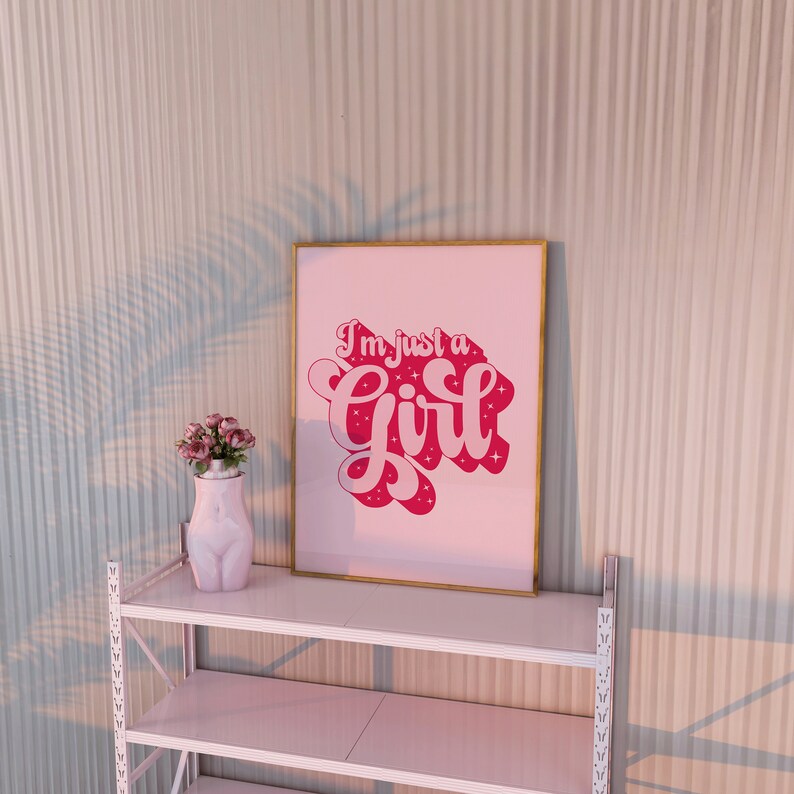 K&ouml;nnte beinhalten: Ein rosa gerahmter Druck mit dem Text "I'm just a girl" in rosa Schrift mit wei&szlig;en Sternen auf rosa Hintergrund.