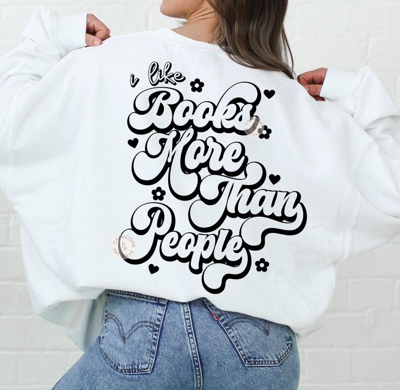 May include: White sweatshirt with the text "I like Books More Than People" in a retro font. The design includes black flowers and hearts. The sweatshirt is a casual, comfortable style.