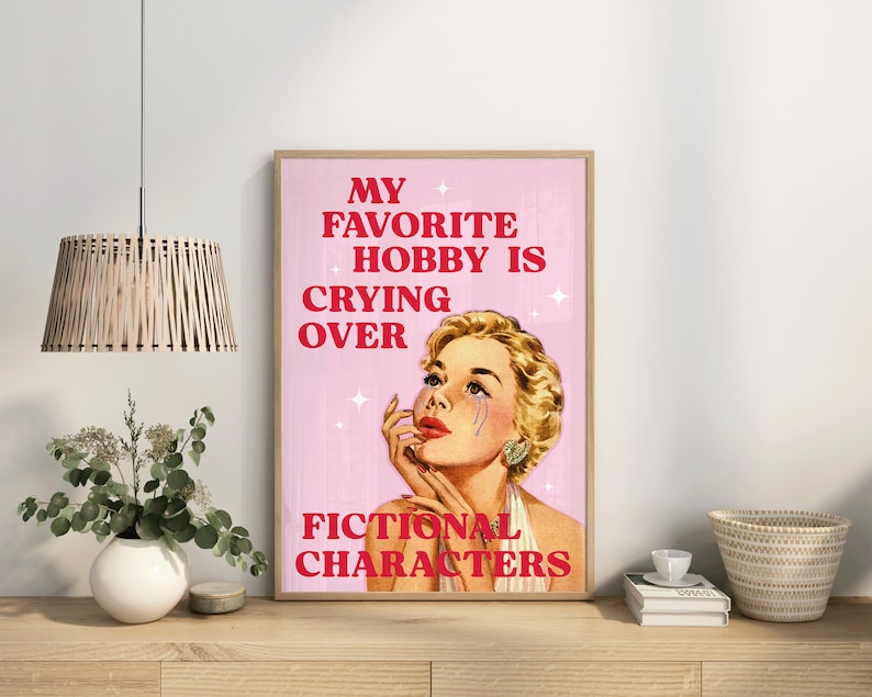 Pode incluir: Um p&ocirc;ster rosa e branco com uma ilustra&ccedil;&atilde;o em estilo retr&ocirc; de uma mulher com uma l&aacute;grima escorrendo pela bochecha. O texto no p&ocirc;ster diz "Meu hobby favorito &eacute; chorar por personagens fict&iacute;cios."