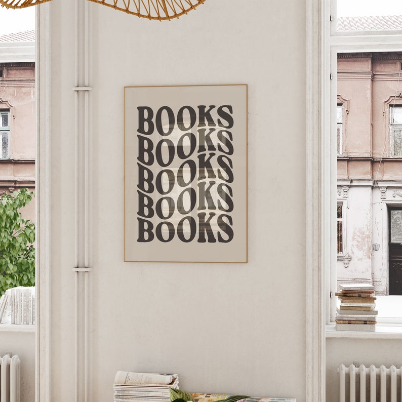 May include: A framed print with the word "BOOKS" repeated five times in a retro, stacked font. The print is in a light brown frame and is hanging on a white wall.