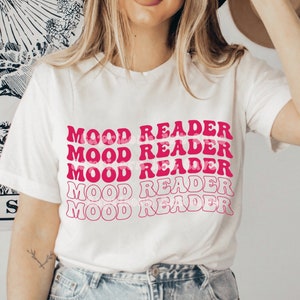 Könnte beinhalten: Ein weißes T-Shirt mit dem Text "MOOD READER" in einem sich wiederholenden, wellenförmigen Design in Rosatönen. Das Shirt ist ein lässiger Stil, der für den Alltag geeignet ist. Das Design hat eine Retro- und Groovy-Ästhetik.