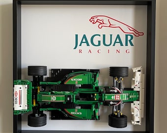 Puede incluir: Un expositor enmarcado con un modelo de coche de Fórmula 1 de Jaguar Racing en verde y blanco. El coche incluye logotipos de patrocinadores como HSBC, Beck's y AT&T, con el número 22 visible. El logotipo de Jaguar y el texto JAGUAR RACING aparecen arriba.