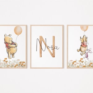 May include: Three Winnie the Pooh themed prints with a watercolour style. The first print features Winnie the Pooh holding a yellow balloon and standing in a field of flowers. The second print features the letter N with the name "Nora" written in cursive. The third print features Winnie the Pooh and Piglet flying in a balloon with a field of flowers in the background.