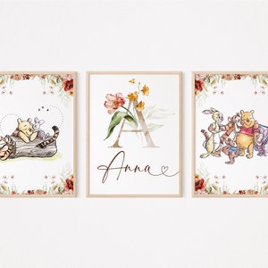 以下が含まれることがあります： 水彩の花の縁取りが施された、くまのプーさんテーマのプリント3枚。最初のプリントは、プーさんとピグレットが木の幹に乗っている様子。2枚目は、水彩の花と「Anna」という名前が書かれた「A」の文字。3枚目は、プーさん、ピグレット、ティガー、イーヨー、ラビットが描かれている。