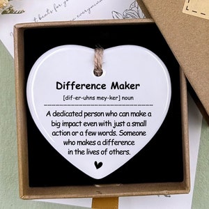 May include: White ceramic heart-shaped ornament with the text "Difference Maker" and a definition of the word. The ornament is in a small brown box with a "Hand made" label.