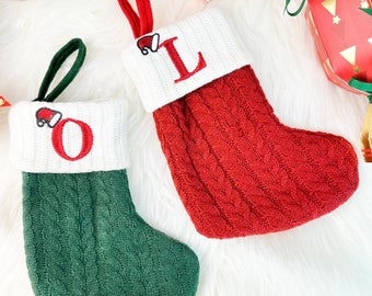 May include: Two Christmas stockings, one red and one green, with white cuffs. The red stocking has the letter "L" embroidered in red, and the green stocking has the letter "O". Both have a small Santa hat detail and a loop for hanging.