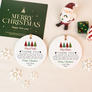 May include: Two white ceramic Christmas ornaments with a tree design and the text "Thank You." A green card with "Merry Christmas" is visible. A Santa figurine and decorative items are also present.