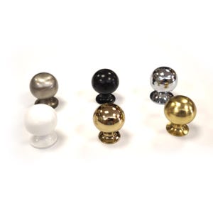 May include: Six spherical cabinet knobs in different finishes are displayed. The knobs include silver, black, gold, chrome, and white. Each knob has a round top and a decorative base. The knobs are shown on a white surface.