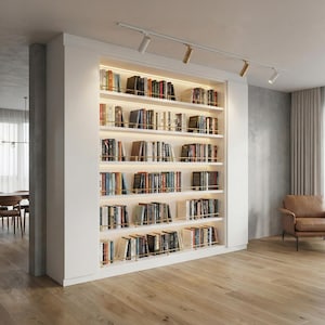 May include: A built-in white bookshelf filled with books of various sizes and colors. The shelves are illuminated with warm lighting, and accented with brass-colored rods. The bookshelf is a prominent feature in a modern living space.